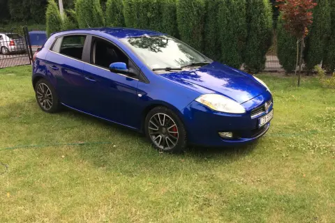 Błękitny Fiat Bravo 1.4 T-Jet zaparkowany na trawniku, za nim żywopłot.