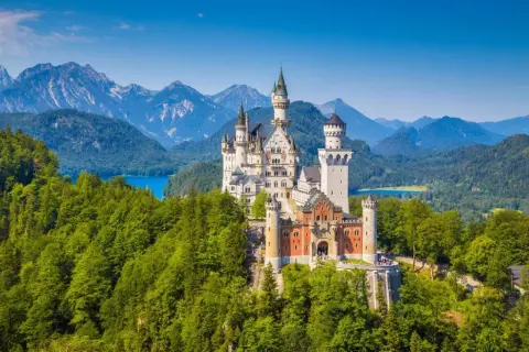 Le château de Neuschwanstein, un joyau parmi le top 10 des plus grands châteaux du monde, se dresse majestueusement sur une colline boisée, dominant un lac bleu et des montagnes imposantes.