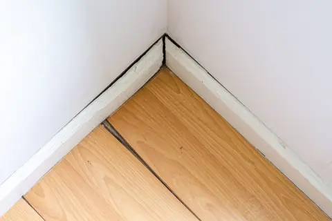 Esquina de habitación con parquet de madera con juntas abiertas. Guía para saber como recuperar el parquet y arreglar estas separaciones.