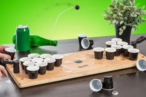 En rolig lekar fest vuxna inomhus med beer pong-spel. En boll flyger mot muggarna på träplattan.
