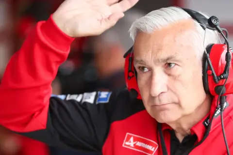 Davide Tardozzi, con auriculares rojos, saluda con la mano. Viste una chaqueta roja de equipo de carreras.