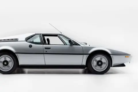 Srebrne BMW M1 E26 widziane z boku, z otwartymi drzwiami.