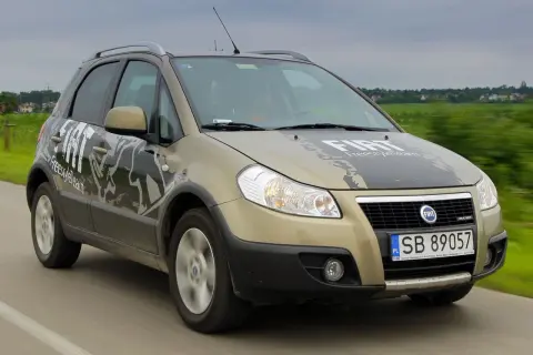 Złoty Fiat Sedici z napisem "FreestyleTeam" na masce i drzwiach jedzie po drodze.