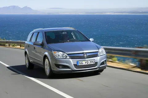 Srebrny Opel Astra H kombi jedzie drogą nad morzem.