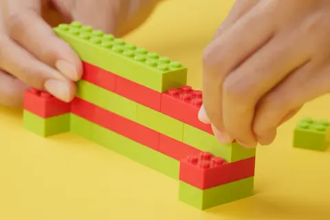 Dziecko buduje z zielonych i czerwonych klocków, pokazując, jak zbudować z klocków lego.