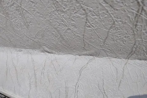 Detaljbild av vit, mönstrad tapet som täcker ett snedtak. Mönstret liknar kvistar eller ådring.