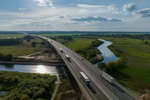 Most na Via Baltica przecina malowniczą dolinę rzeki, po której płyną ciężarówki.