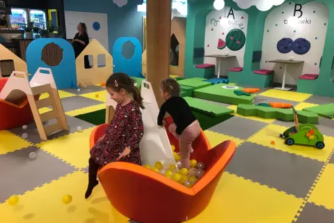 Dwie dziewczynki bawią się w sali zabaw Smart Kids Planet Warszawa. Jedna zjeżdża po zjeżdżalni do basenu z piłeczkami.