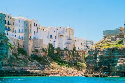 La famosa spiaggia di Polignano a Mare, con case bianche aggrappate alle scogliere e bagnanti che si godono il mare cristallino.