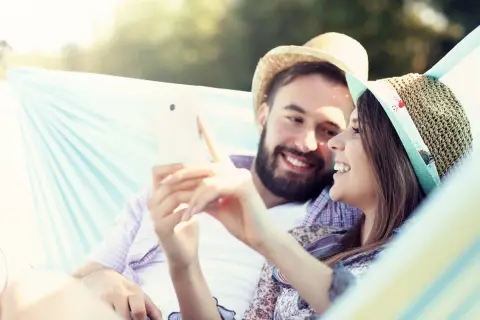 Para udowodnić dziewczynie że ją kocham przez sms, wystarczy szczery uśmiech i wspólne chwile. Para w hamaku cieszy się sobą, przeglądając telefon.