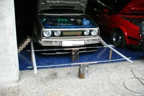 Selbstgemachte Achsvermessung: Ein silberner VW Golf mit geöffneter Haube steht bereit. Daneben ein roter Wagen.