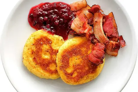 Två gyllene potatisbullar med knaperstekt bacon och rårörda lingon. Ett klassiskt potatisbullar recept som passar perfekt till helgfrukosten.