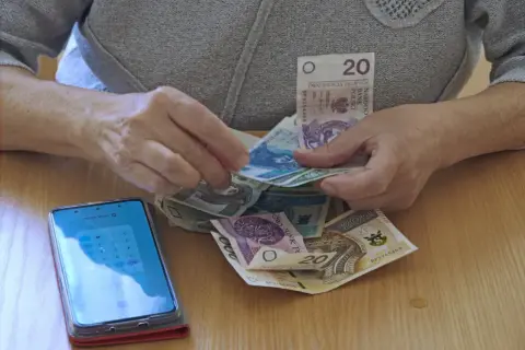 Dłonie liczą pieniądze, obok leży smartfon z kalkulatorem. Czy to dodatek pielęgnacyjny z ZUS, komu przysługuje?