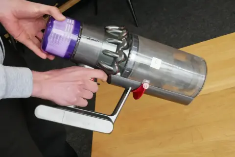 Ręce demontują fioletowy filtr z odkurzacza Dyson, przygotowując go do czyszczenia filtra magnetycznego.