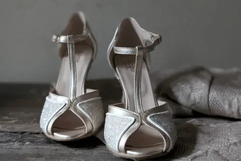 Scarpe dorate con glitter e cinturino a T, perfette da abbinare a un abito in pizzo per un look da cerimonia.