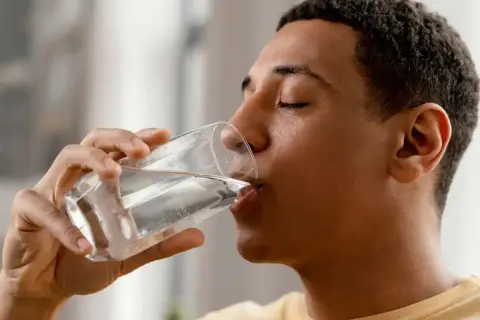 Un jeune homme boit un verre d'eau minérale magnésium, une boisson rafraîchissante et bénéfique.