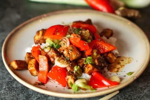 Leckeres, klebriges Tofu-Rezept mit Reis, Paprika und Frühlingszwiebeln, garniert mit Kräutern.