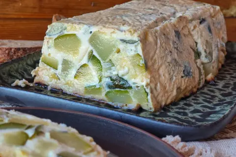 Pastel de calabacín casero, con trozos verdes visibles en una masa dorada, servido en plato oscuro.