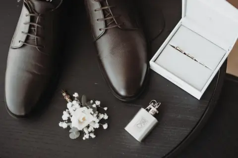 Eleganckie, brązowe oksfordy – jeden z klasycznych rodzajów butów męskich. Obok butonierka, obrączki i piersiówka.