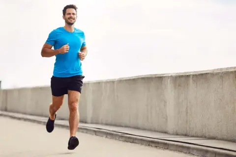 Lächelnder Mann joggt auf einer Straße, baut beim Joggen Muskeln auf.