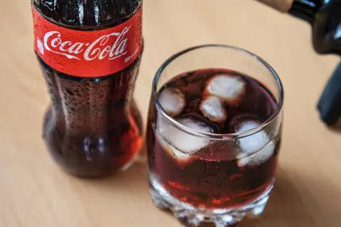 Szklanka z lodem i napojem, obok butelka Coca-Coli. Czerwone wino z colą w szklance, orzeźwiające.