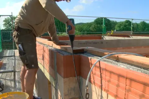 Handwerker arbeitet am dachstuhl aufbau. Mit Akkuschrauber werden Holzbalken befestigt.