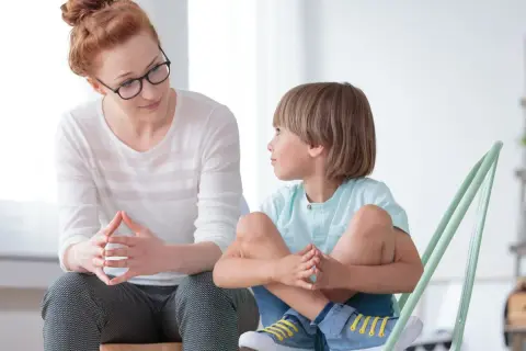 Kobieta z okularami i chłopiec siedzą naprzeciwko siebie, rozmawiając. To przykład, jak rozmawiać z dzieckiem autystycznym, budując zaufanie.