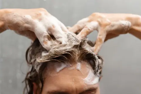 Manos con espuma masajean el cuero cabelludo, demostrando cómo lavarse el pelo correctamente para una limpieza profunda y un cabello saludable.