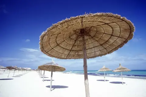 Słomiane parasole na białej plaży, idealne na upalną tunezyjską pogodę w sierpniu. Błękitne niebo i morze.