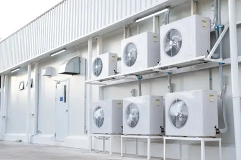 Rzędy białych jednostek klimatyzacyjnych zamontowanych na ścianie białego budynku.