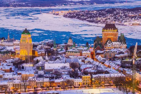 Quebec Winter: Eisbedeckter Sankt-Lorenz-Strom und schneebedeckte Dächer der Altstadt, beleuchtet vom Abendlicht.