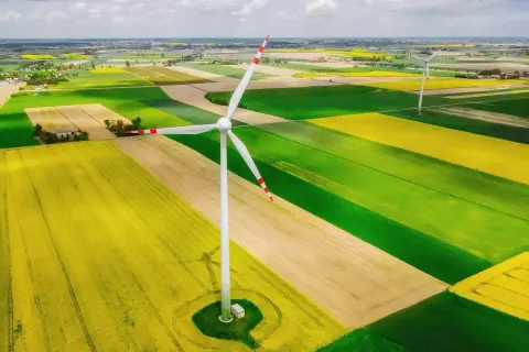 Wiatrak na tle pól rzepaku i zbóż. Nowa ustawa wiatrakowa wspiera takie inwestycje w zieloną energię.