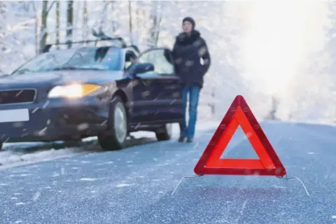 Gefährliche Straße: Ein Auto mit Warnblinker, eine Person und ein Warndreieck im Schnee. So entsteht Blitzeis.