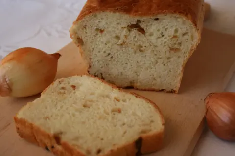 Pyszny chleb cebulowy na drożdżach, świeżo upieczony, z widocznymi kawałkami cebuli w miękiszu. Obok leżą całe cebule.