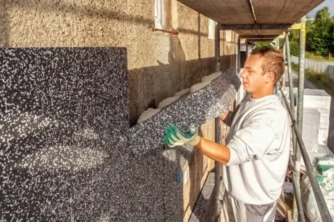 Pracownik montuje styropian na ścianie starego domu, zapobiegając wilgoci i poprawiając izolację.