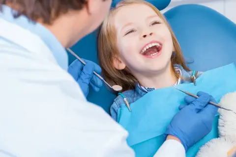 Uśmiechnięta dziewczynka u dentysty, która ma krzywy zgryz. Lekarz bada jej zęby.