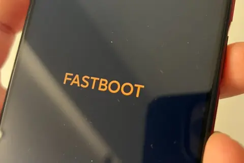 Pomarańczowy napis FASTBOOT na ciemnym ekranie telefonu, trzymanego w dłoni.