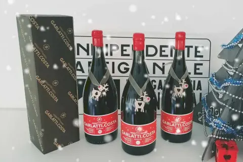 Tre bottiglie di birra Garlatti.Costa con decorazioni natalizie, una scatola e un albero di Natale sullo sfondo.