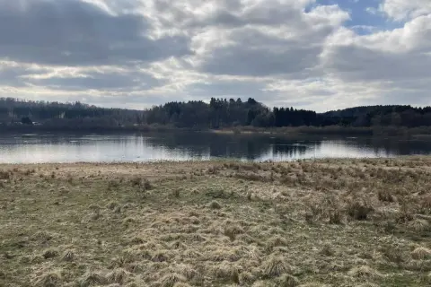 Ein ruhiger Blick auf den Krombachtalsperre Rundweg mit bewaldeten Ufern und einem Himmel voller Wolken.