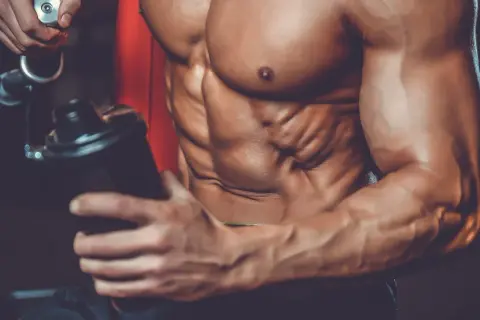 Atleta con addominali scolpiti prepara un frullato, mostrando a cosa servono le proteine in polvere palestra per la crescita muscolare.
