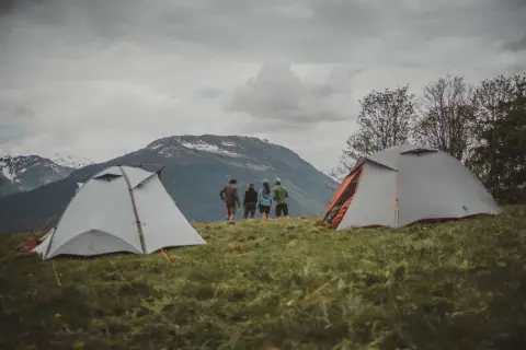 Dwa namioty na trawiastym zboczu górskim, z ludźmi stojącymi w tle.