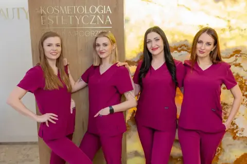 Cztery kobiety w uniformach medycznych stoją obok siebie przed tablicą z napisem "Kosmetologia Estetyczna".