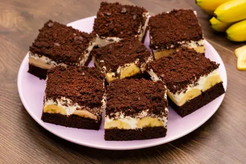 Saftiger Maulwurfkuchen vom Blech mit Bananen und Schokostreuseln auf einem rosa Teller.