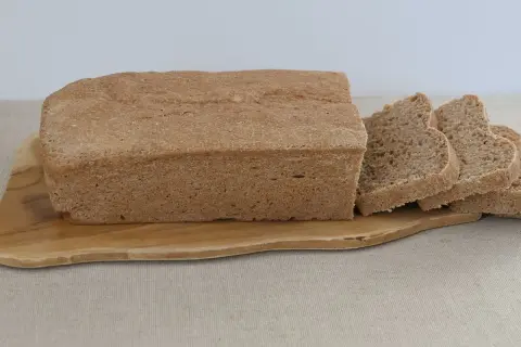 Bochenek chleba graham pokrojony na kromki, leżący na drewnianej desce.