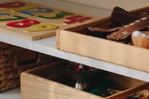 Drewniane pudło na zabawki z pluszowym piernikiem i kuleczkami. Obok puzzle z cyframi i wiklinowy kosz.