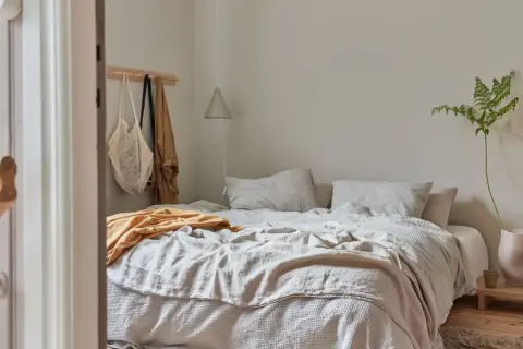 Sovrum med en bäddad säng i olika nyanser av beige. En gul filt ligger överst. Frågan "hur blandar man beige" besvaras här med en lugn och harmonisk inredning.