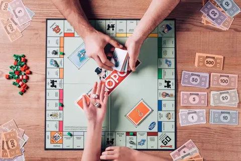 Ręce graczy dzielą pieniądze Monopoly na planszy gry, obok kostek i żetonów.