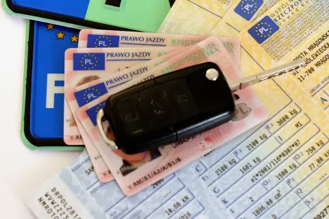 Kluczyki do auta i dokumenty, w tym prawo jazdy. Czy prawo jazdy jest bezterminowe? Na zdjęciu widać też dowód rejestracyjny i tablicę.
