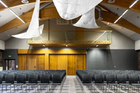Nowoczesna sala konferencyjna z rzędami czarnych krzeseł, drewnianymi elementami i kamienną ścianą. Idealne miejsce na konferencje na Mazurach.