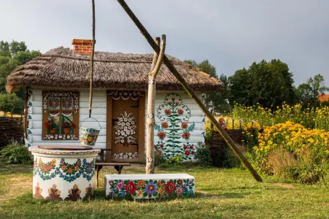 Malowana chata z łubą i studnią, ozdobiona kwiatami. Warto zobaczyć Zalipie i okolice, by podziwiać ludową sztukę.